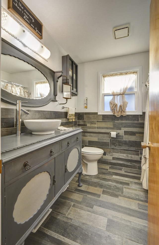 bathroom featuring toilet, a wainscoted wall, wood finished floors, vanity, and tile walls