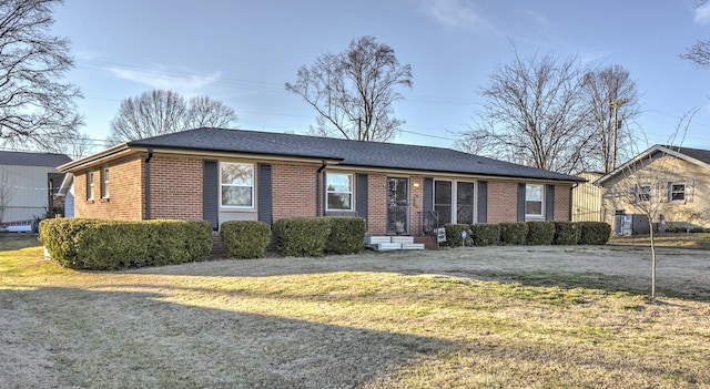 single story home featuring a shingled roof, a front yard, and brick siding