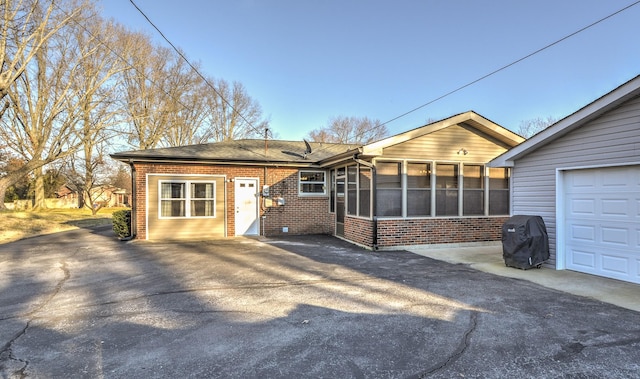 view of front facade featuring a garage, a sunroom, brick siding, and driveway