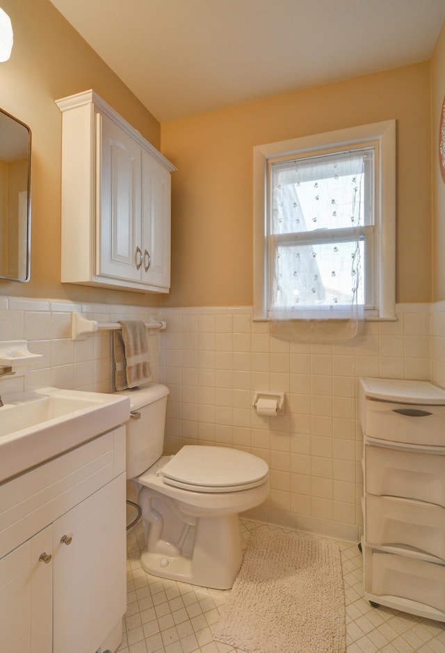 bathroom with a wainscoted wall, tile walls, toilet, vanity, and tile patterned floors