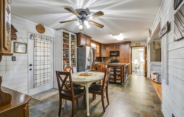 dining room with a ceiling fan, stone finish flooring, and wood walls