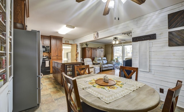 dining room with ceiling fan, stone finish flooring, and wooden walls