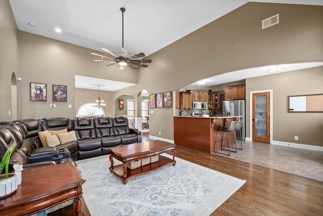 living room featuring arched walkways, visible vents, wood finished floors, high vaulted ceiling, and ceiling fan with notable chandelier