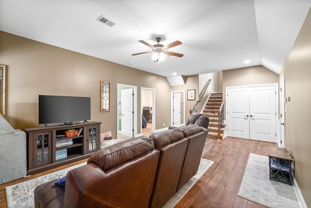 living room featuring lofted ceiling, wood finished floors, visible vents, a ceiling fan, and stairway