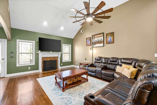 living room featuring baseboards, ceiling fan, wood finished floors, a fireplace, and high vaulted ceiling