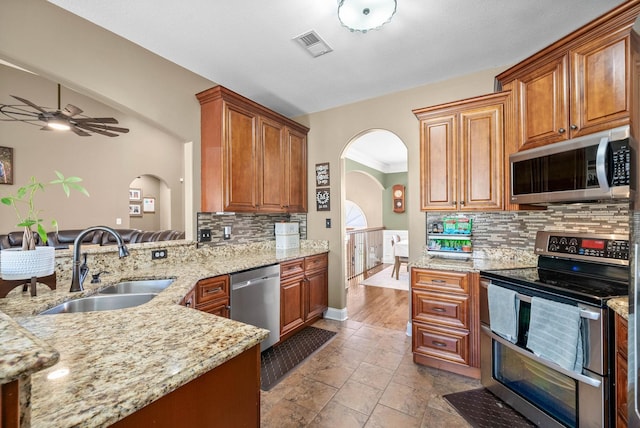 kitchen featuring light stone counters, arched walkways, visible vents, appliances with stainless steel finishes, and a sink