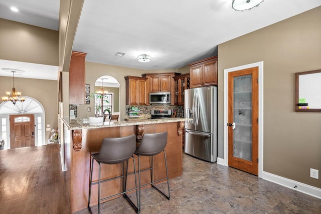 kitchen with brown cabinets, decorative backsplash, appliances with stainless steel finishes, a chandelier, and a kitchen breakfast bar