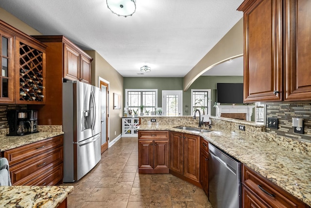 kitchen with backsplash, appliances with stainless steel finishes, a sink, light stone countertops, and a peninsula