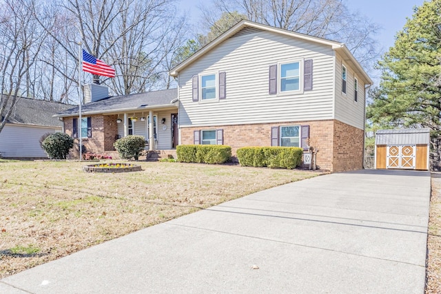 split level home featuring a chimney, a front lawn, an outbuilding, and brick siding