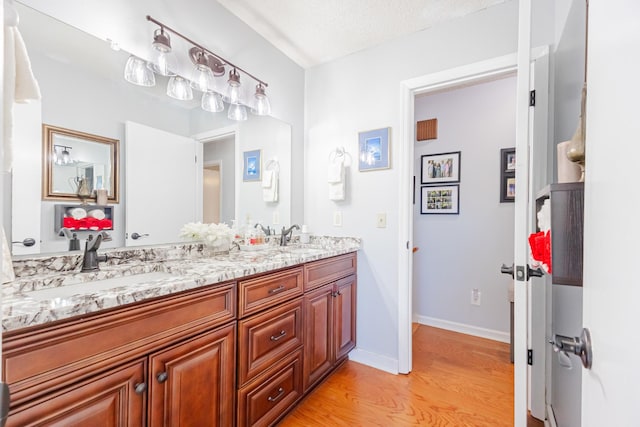 bathroom featuring double vanity, wood finished floors, a sink, and baseboards