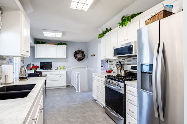 kitchen featuring light floors, stainless steel appliances, backsplash, white cabinets, and a sink