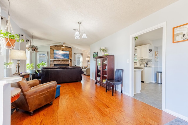 living area featuring vaulted ceiling, a brick fireplace, a chandelier, and light wood-style flooring