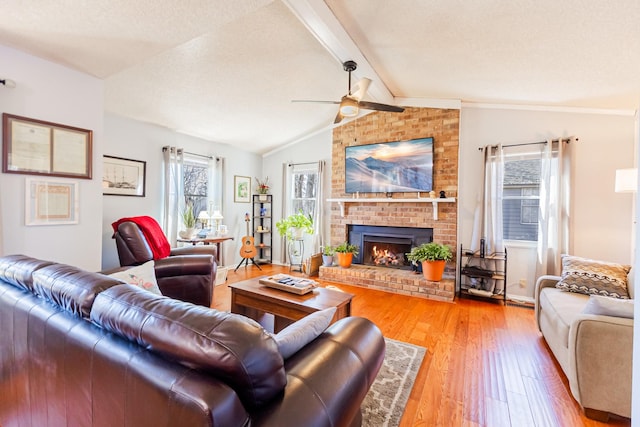 living room with lofted ceiling with beams, a brick fireplace, light wood-type flooring, and a textured ceiling