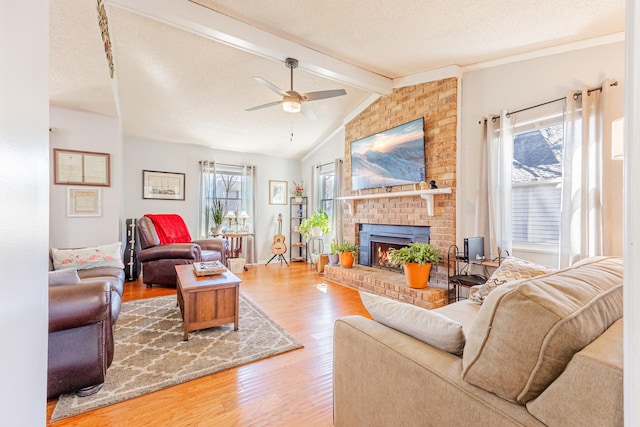 living area featuring vaulted ceiling with beams, a textured ceiling, wood finished floors, a ceiling fan, and a brick fireplace