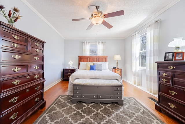 bedroom featuring baseboards, visible vents, wood finished floors, a textured ceiling, and crown molding