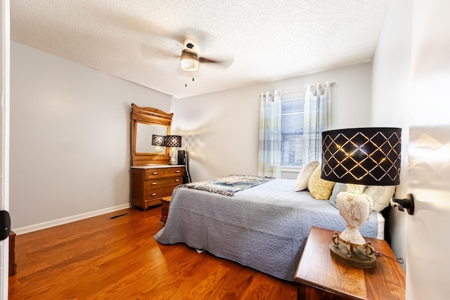 bedroom with a textured ceiling, wood finished floors, visible vents, a ceiling fan, and baseboards