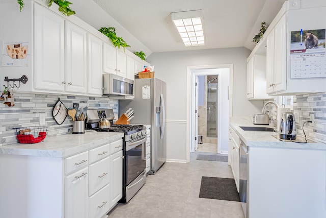 kitchen with stainless steel appliances, light countertops, backsplash, white cabinets, and a sink