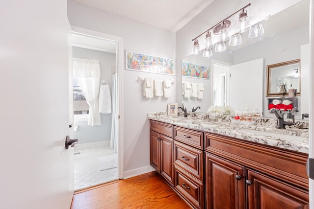 full bathroom with double vanity, a sink, baseboards, and wood finished floors