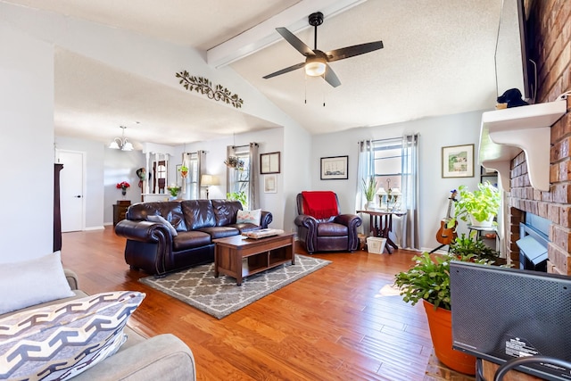 living area featuring vaulted ceiling with beams, a fireplace, wood finished floors, and ceiling fan with notable chandelier