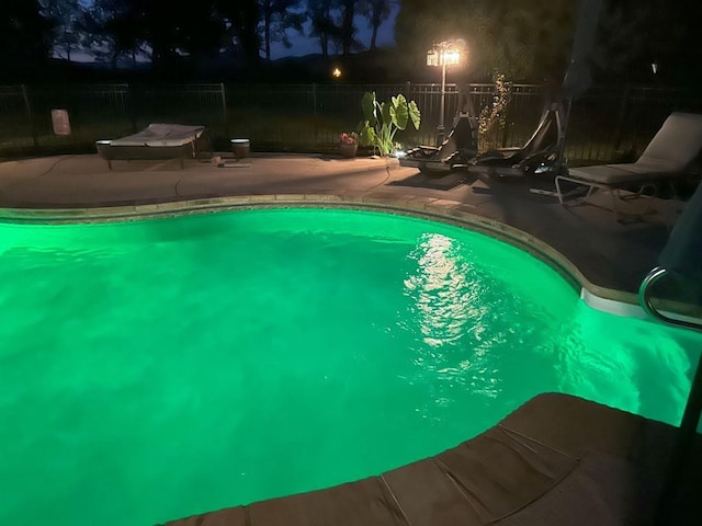 pool at night featuring fence, a fenced in pool, and a patio