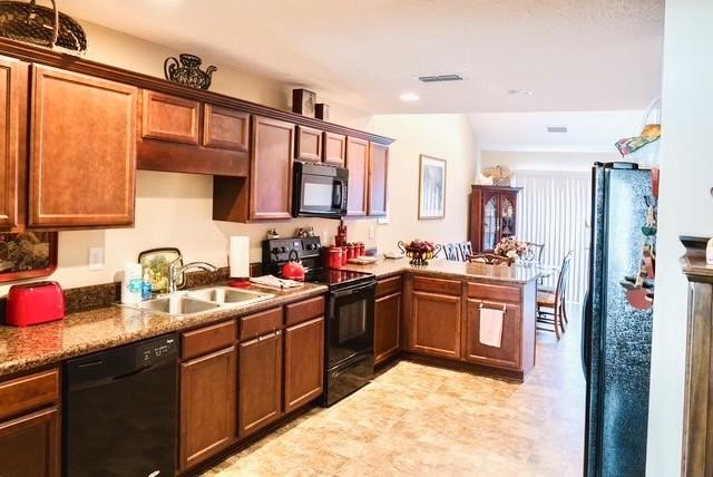 kitchen with visible vents, black appliances, a sink, a peninsula, and vaulted ceiling