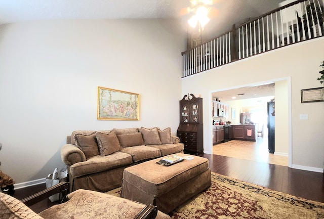 living area with baseboards, a high ceiling, a ceiling fan, and light wood-style floors