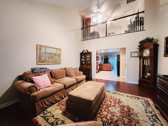 living area with wood finished floors, visible vents, baseboards, a high ceiling, and ceiling fan