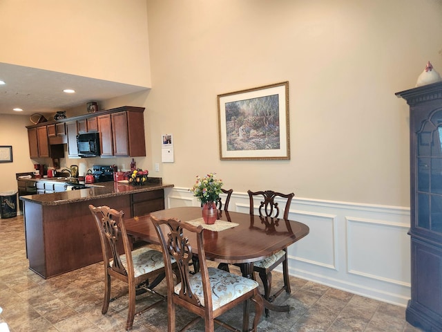 dining space featuring recessed lighting, a decorative wall, a towering ceiling, and a wainscoted wall