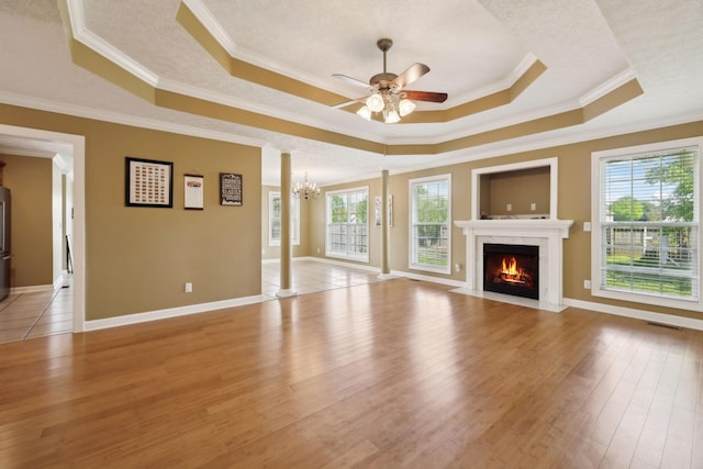 unfurnished living room featuring light wood finished floors, ceiling fan with notable chandelier, a fireplace with flush hearth, and a tray ceiling