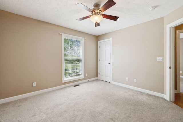 spare room featuring light colored carpet, ceiling fan, baseboards, visible vents, and a textured ceiling