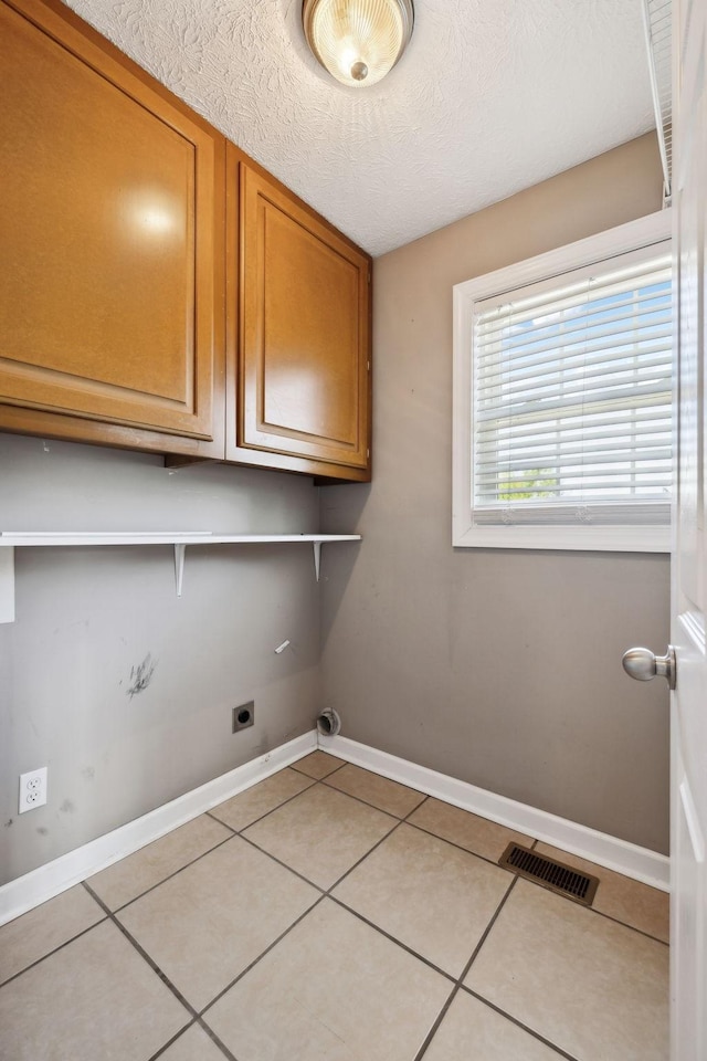 clothes washing area featuring electric dryer hookup, cabinet space, baseboards, visible vents, and light tile patterned flooring