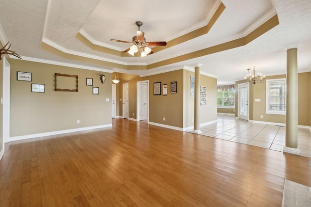 unfurnished room with decorative columns, a raised ceiling, ceiling fan with notable chandelier, and crown molding