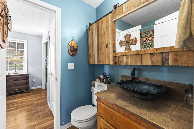 bathroom featuring toilet, vanity, a textured ceiling, wood finished floors, and baseboards