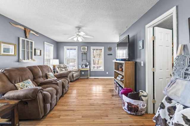 living room with a textured ceiling, ceiling fan, light wood-style flooring, and baseboards