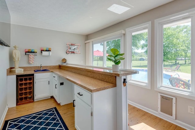 kitchen featuring light wood finished floors, light countertops, white cabinetry, a sink, and a peninsula