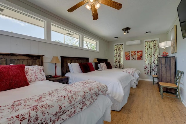 bedroom featuring light wood-type flooring, ceiling fan, baseboards, and an AC wall unit