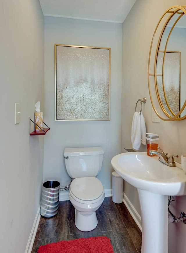 half bathroom with wood finished floors, toilet, and baseboards