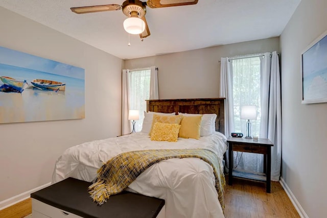 bedroom with ceiling fan, multiple windows, baseboards, and wood finished floors