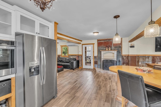 kitchen with appliances with stainless steel finishes, light wood-style floors, a large fireplace, wainscoting, and white cabinetry