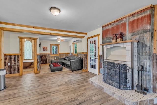 living area featuring a wainscoted wall, a fireplace, a wall mounted AC, a ceiling fan, and wood finished floors