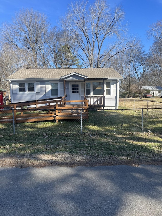 view of front facade featuring a shingled roof, fence, and a front lawn