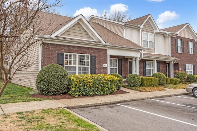 view of front of property with uncovered parking, brick siding, and a shingled roof