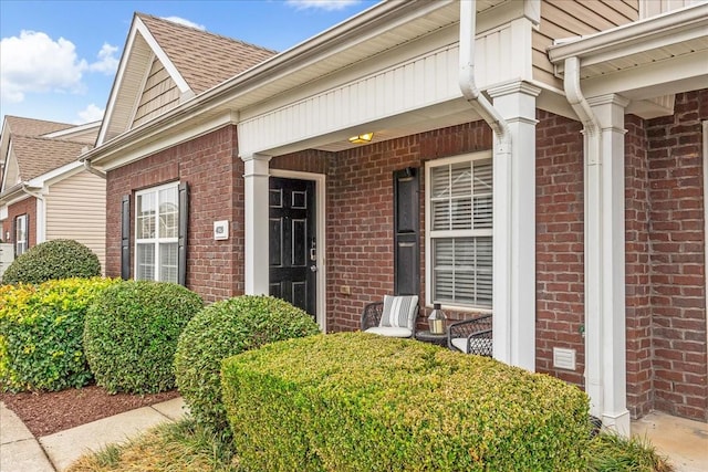 property entrance with a shingled roof, covered porch, and brick siding