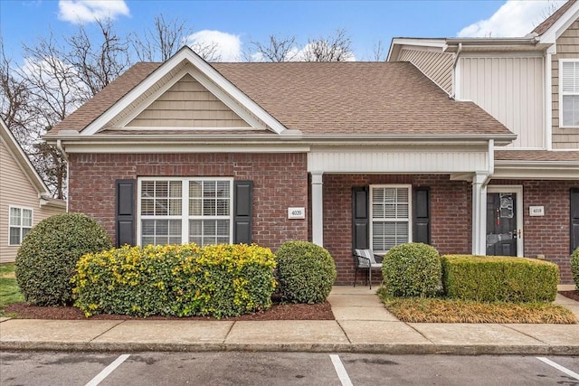 view of front of home featuring roof with shingles, uncovered parking, a porch, and brick siding