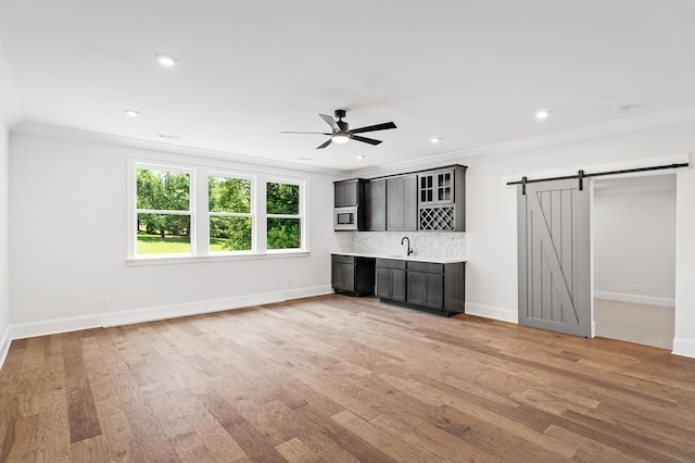 unfurnished living room featuring ornamental molding, a barn door, a sink, and light wood-style floors