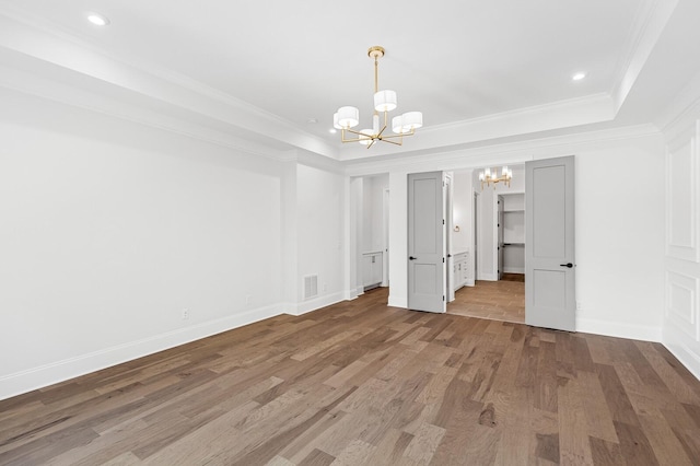 unfurnished room featuring a tray ceiling, visible vents, an inviting chandelier, ornamental molding, and wood finished floors