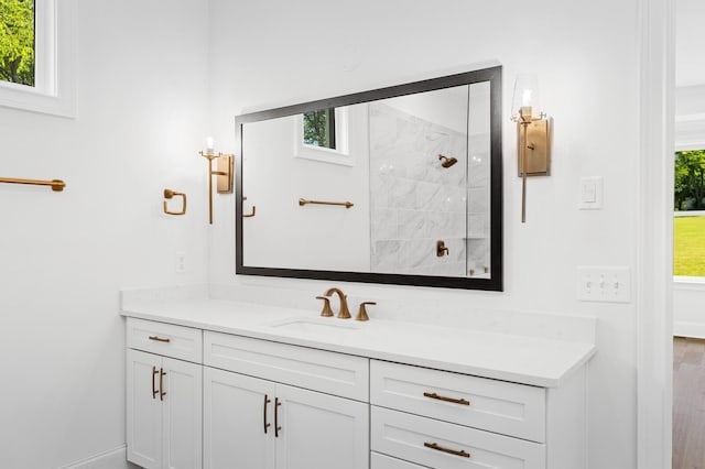 bathroom with a tile shower, vanity, and baseboards