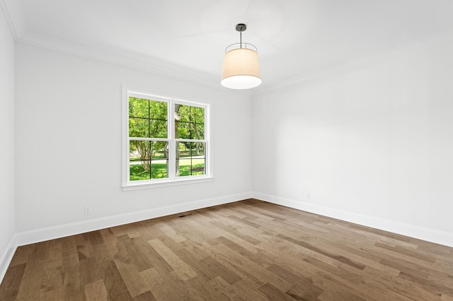 empty room with crown molding, wood finished floors, and baseboards