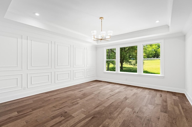 unfurnished room featuring a notable chandelier, wood finished floors, baseboards, ornamental molding, and a raised ceiling