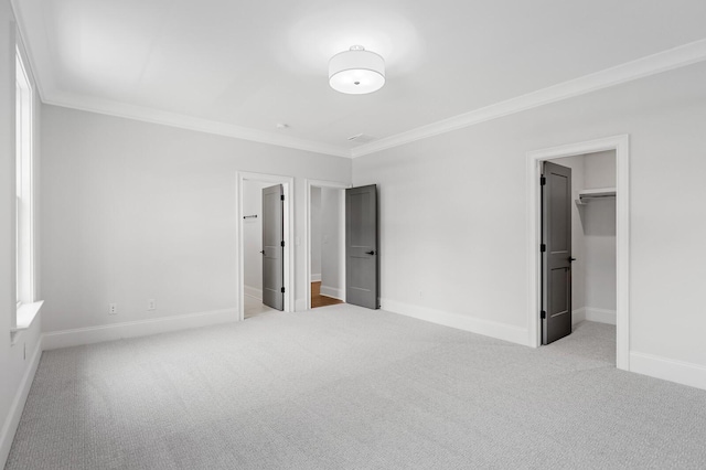 unfurnished bedroom featuring carpet, ornamental molding, a walk in closet, and baseboards